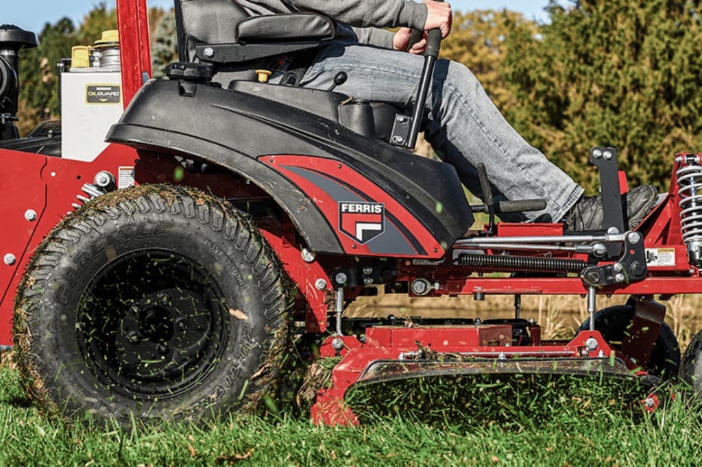 Action shot of a red and black Ferris zero-turn mower cutting grass, with the Ferris logo on the side panel and clippings discharging from the deck