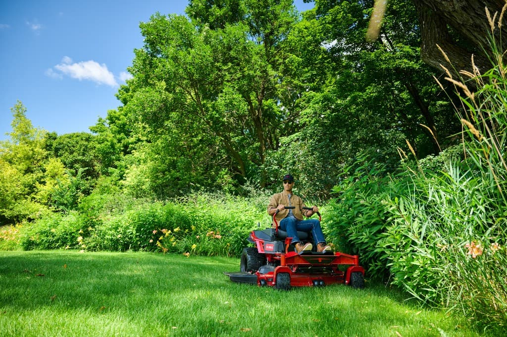 Operator driving a red Toro zero-turn mower on a manicured green lawn